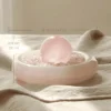 stone-blessings-rose-quartz-sphere-resting-on-a-bed-of-rose-quartz-chips-in-an-afghan-pink-marble-bowl-styled-on-a-linen-runner-with-size Rose Quartz Sphere in Pink Marble Vessel styled on linen with size reference