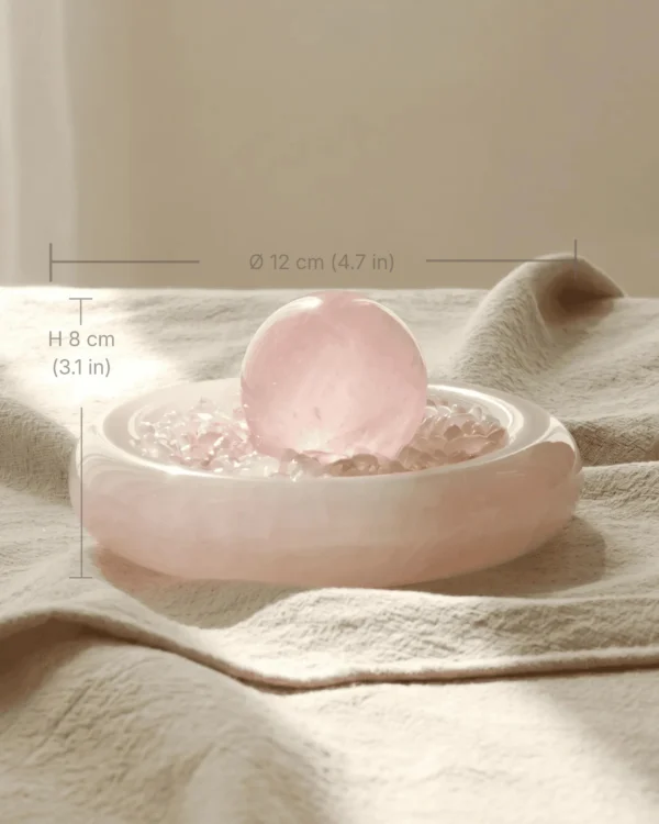 stone-blessings-rose-quartz-sphere-resting-on-a-bed-of-rose-quartz-chips-in-an-afghan-pink-marble-bowl-styled-on-a-linen-runner-with-size Rose Quartz Sphere in Pink Marble Vessel styled on linen with size reference