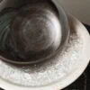 Stone Blessings close up of a polished obsidian sphere resting on clear quartz chips in a travertine pedestal bowl