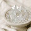 stone-blessings-close-up-of-clear-quartz-towers-rising-from-clear-quartz-chips-in-a-travertine-pedestal-bowl-on-soft-cream-fabric Stone Blessings close up of clear quartz towers rising from clear quartz chips in a travertine pedestal bowl on soft cream fabric