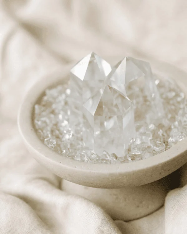 stone-blessings-close-up-of-clear-quartz-towers-rising-from-clear-quartz-chips-in-a-travertine-pedestal-bowl-on-soft-cream-fabric Stone Blessings close up of clear quartz towers rising from clear quartz chips in a travertine pedestal bowl on soft cream fabric
