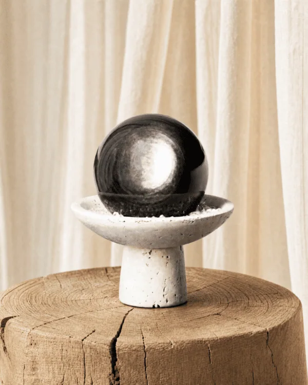 Stone Blessings obsidian sphere centerpiece styled on a raw wood log with soft cream curtains in a quiet natural setting