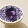 Stone Blessings polished amethyst sphere resting in a stone bowl of chevron amethyst chips angled view