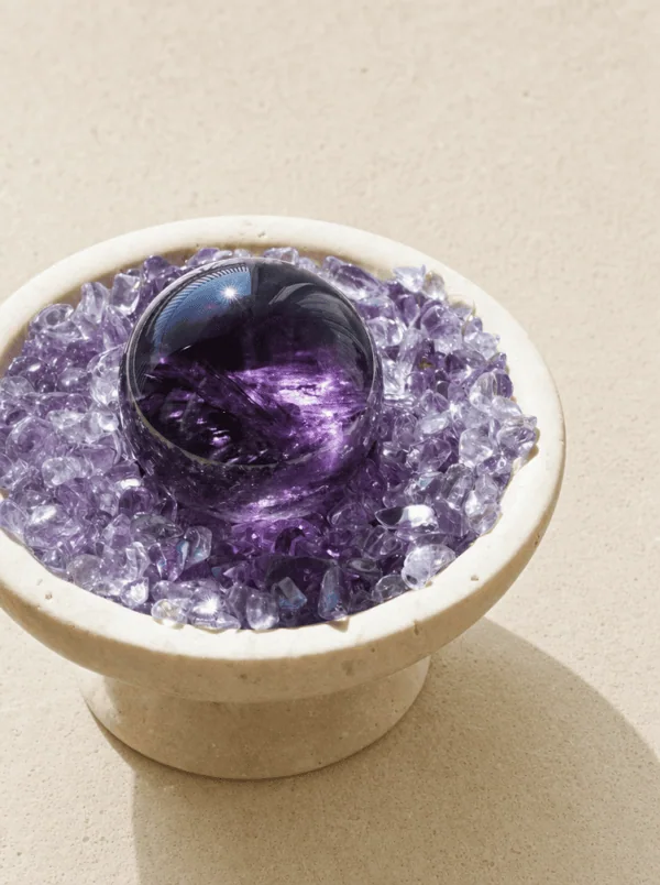 Stone Blessings polished amethyst sphere resting in a stone bowl of chevron amethyst chips angled view