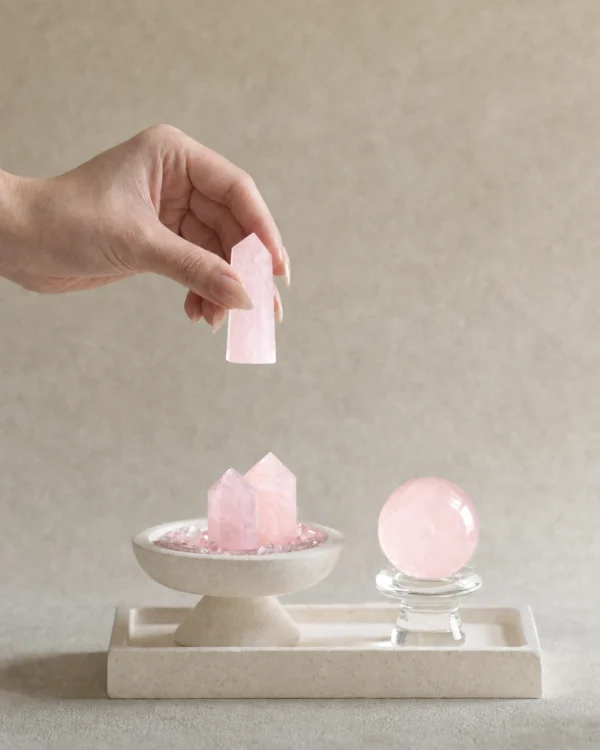 Stone Blessings rose quartz centerpiece shown with a hand placing a rose quartz tower into the travertine pedestal bowl
